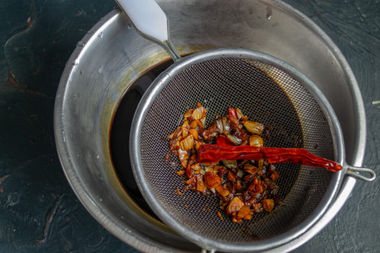 Straining the teriyaki sauce through a sieve to remove garlic and chili pieces.