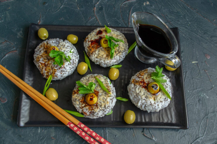 Finished rice balls arranged on a plate, being garnished with olives and green onions.