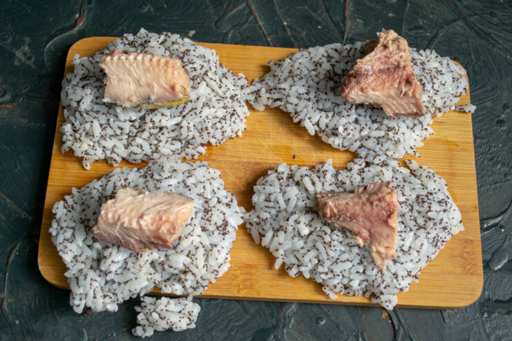 A piece of canned fish being placed on a flat rice patty.