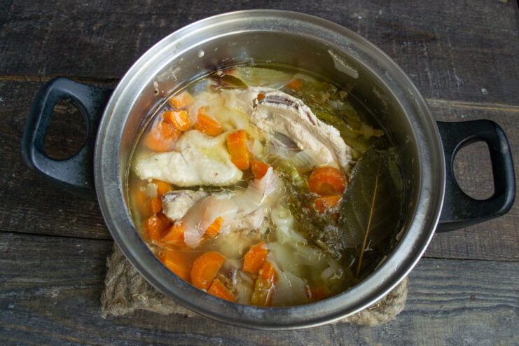 Simmering the Broth to Develop Deep Flavors A pot of chicken broth with vegetables simmering on a stove.