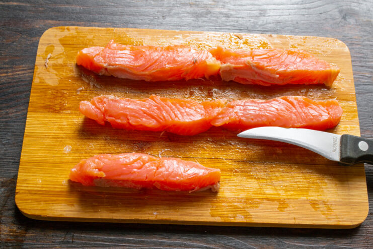 Preparing the Salmon for Sushi Rolls Close-up of a salmon fillet being sliced into long strips for sushi rolls.