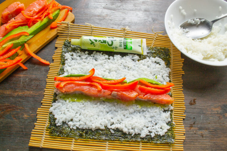 Adding a Crunchy Bell Pepper Strips of red bell pepper being added to the other fillings on the sushi rice.