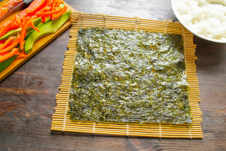 Starting the Sushi Roll Assembly A sheet of dark green nori seaweed placed on a bamboo rolling mat.
