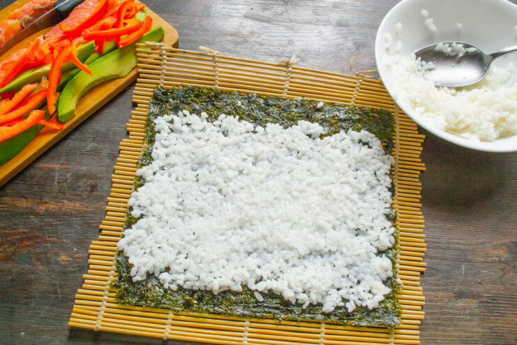 Spreading the Sushi Rice on Nori Hands spreading a thin, even layer of sushi rice over a nori sheet.