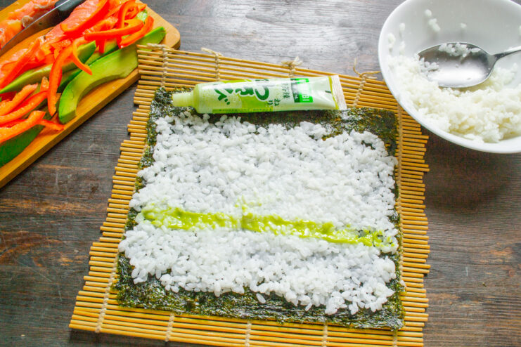 Adding a Kick with Wasabi A thin line of green wasabi paste being squeezed onto the sushi rice.