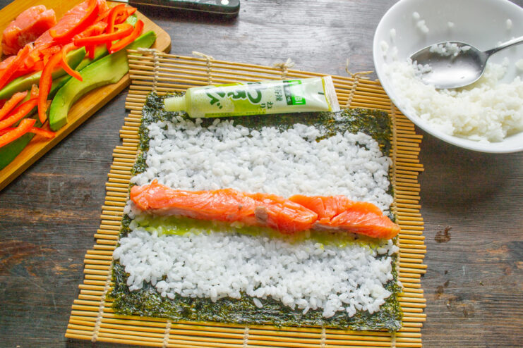 Placing the Salmon Filling Strips of pink salmon being placed on the sushi rice next to the wasabi line.