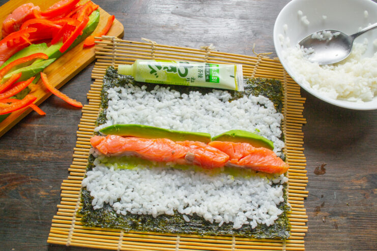 Adding Creamy Avocado Slices Slices of green avocado being arranged next to the salmon on the sushi rice.