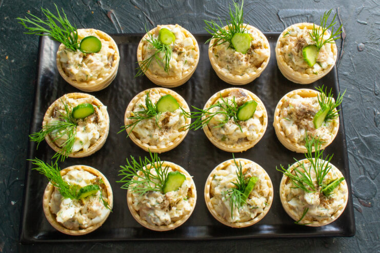 Garnishing Tartlets with Fresh Cucumber and Dill Finished salmon salad tartlets being garnished with thin slices of fresh cucumber.