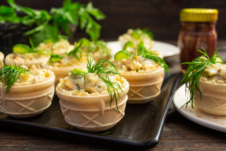 A platter of salmon and anchovy salad served in crispy tartlets, garnished with dill and cucumber.