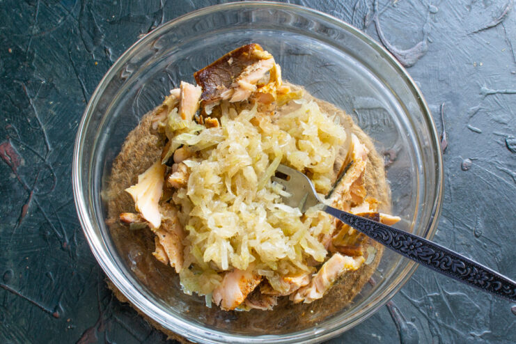 Combining Flaked Salmon with Sautéed Onions Cooled sautéed onions being added to a bowl of flaked salmon.