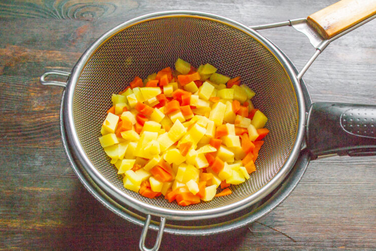 Step 2: Draining the cooked vegetables to cool them down. Cooked diced potatoes and carrots being drained in a metal sieve.