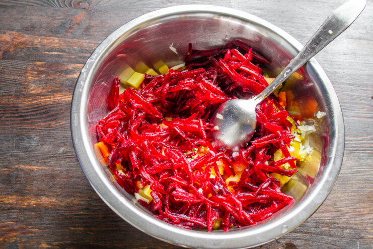 Step 7: Grating cooked beetroot for the salad's signature color. Cooked beetroot being grated on a coarse grater into a bowl.