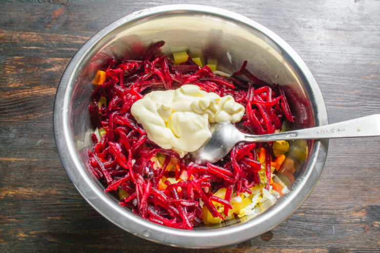 Step 8: Dressing the salad with creamy mayonnaise. A spoonful of mayonnaise being added to the bowl of salad ingredients.