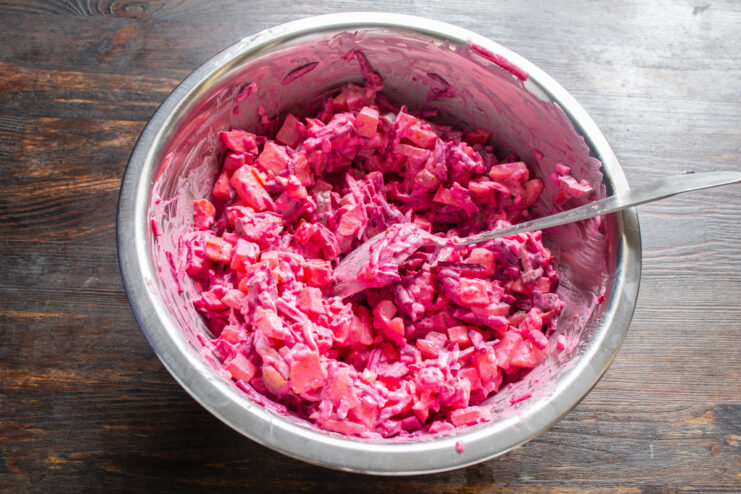 Step 9: Mixing the salad until everything is beautifully pink. Mixing the Barbie Beetroot Salad in a glass bowl, all ingredients turning pink.