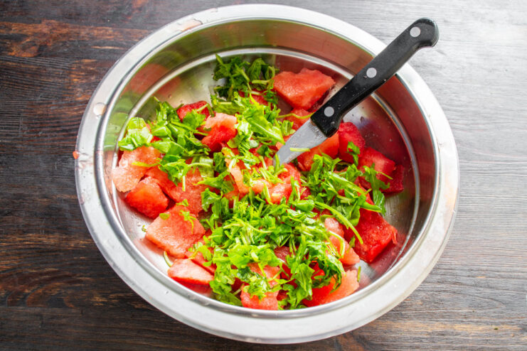 Fresh mint adds a cool, aromatic touch to the watermelon salad. Chopped fresh mint being added to a bowl of watermelon cubes.