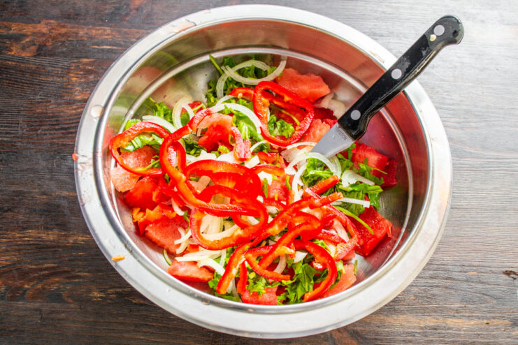 Bright red bell peppers add sweetness and a crunchy texture. Sliced red bell pepper being added to the bowl with watermelon and onion.