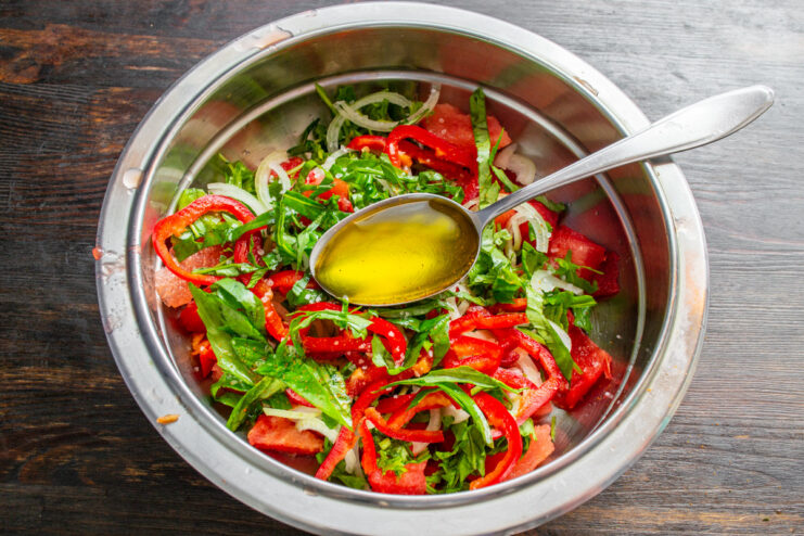 Toss gently to combine all ingredients without crushing the watermelon. Mixing the watermelon salad with seasonings in a white bowl using spoons.