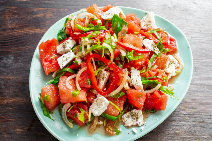 Serve immediately after seasoning for the best taste and texture. The finished watermelon salad in a bowl, being seasoned with black pepper from a grinder.