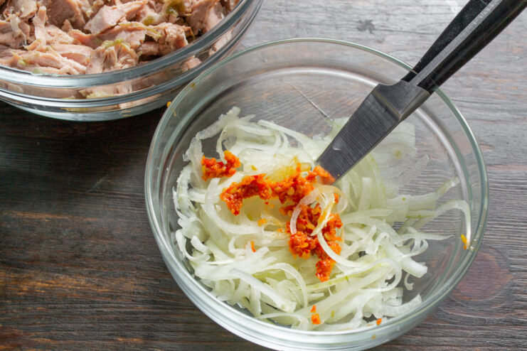 Adding Spicy Adjika to the Onions A spoonful of red adjika paste being added to a bowl of sliced onions.