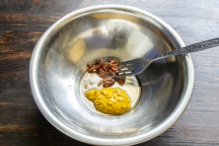 Mashing anchovy fillets to create a flavorful base for the salad dressing. Mashing anchovy fillets with a fork in a small bowl.