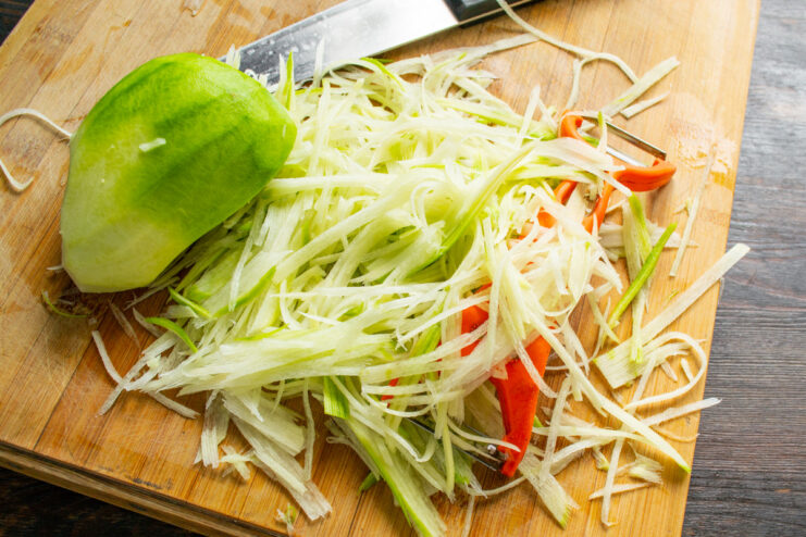 Grating the green radish for the salad base Grating a green radish on a coarse grater into a bowl.