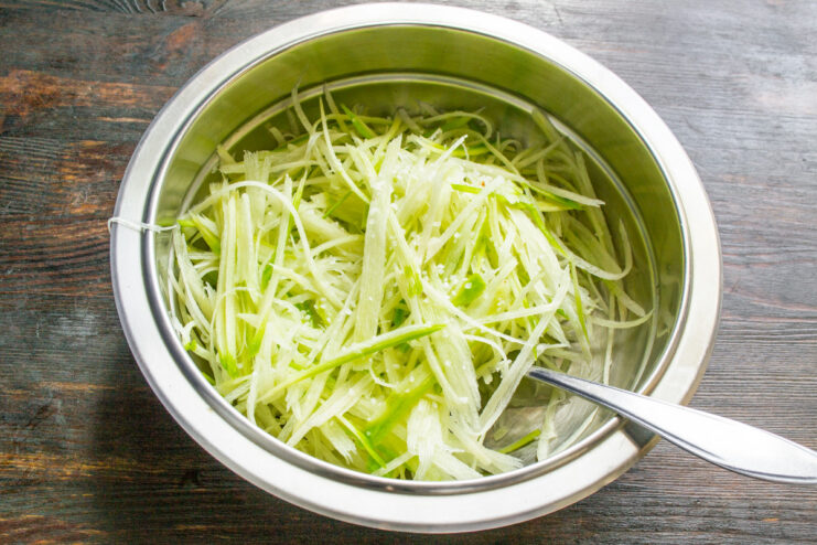 Salting the grated radish to soften it and draw out moisture Sprinkling coarse sea salt over a bowl of grated green radish.