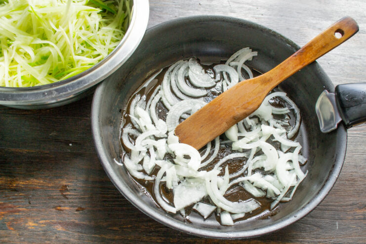 Slicing an onion into thin half-rings for frying A large onion being sliced into thin half-rings on a cutting board.