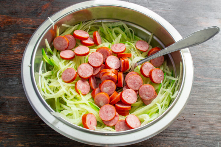 Slicing smoked sausage for the salad Smoked sausage being cut into thin, round slices on a cutting board.
