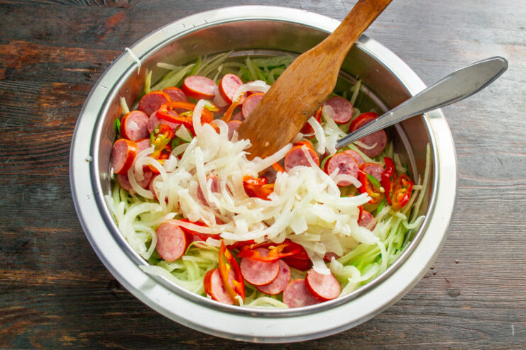 Adding cooled fried onions to the salad ingredients Adding cooled, translucent fried onions to the bowl with grated radish.