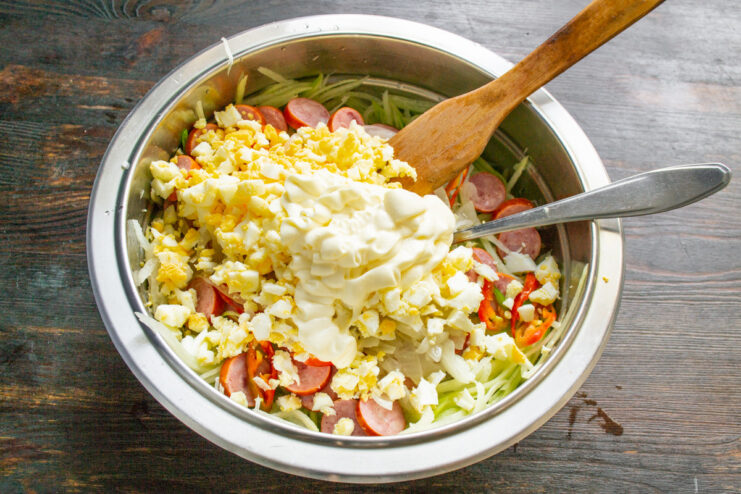 Dressing the salad with creamy mayonnaise Adding a generous dollop of mayonnaise to the salad ingredients in a bowl.