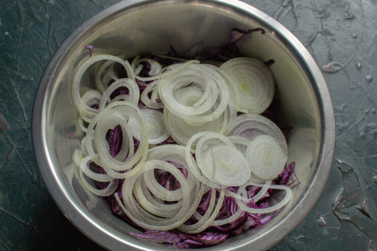Slicing Sweet Onion into Thin Rings for a Milder Flavor A hand slicing a sweet white onion into thin rings on a cutting board.