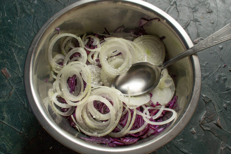 Massaging Cabbage and Onions to Soften Them and Release Juices Hands in gloves massaging shredded red cabbage and onions in a bowl.