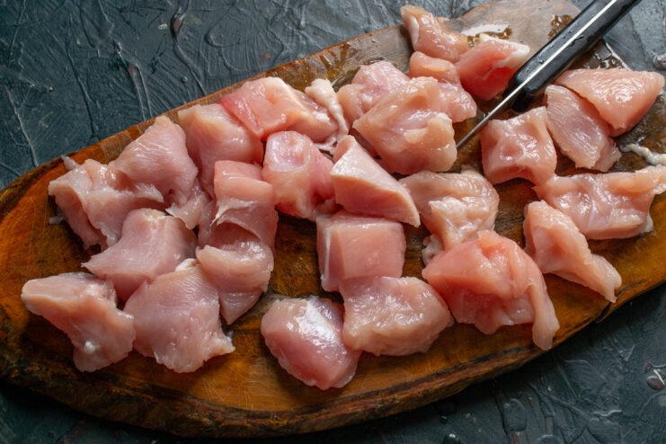 Preparing the Turkey Breast by Dicing it into Bite-Sized Cubes Raw turkey breast being diced into cubes on a cutting board.