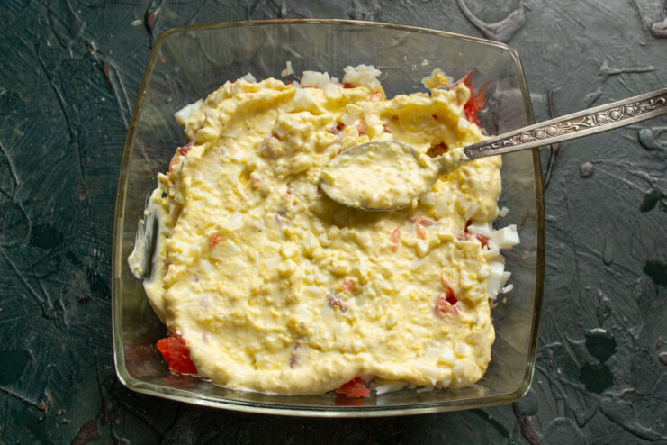 Spreading the creamy mayonnaise sauce over the salad layers. Spreading a smooth, even layer of mayonnaise dressing over the salad ingredients.