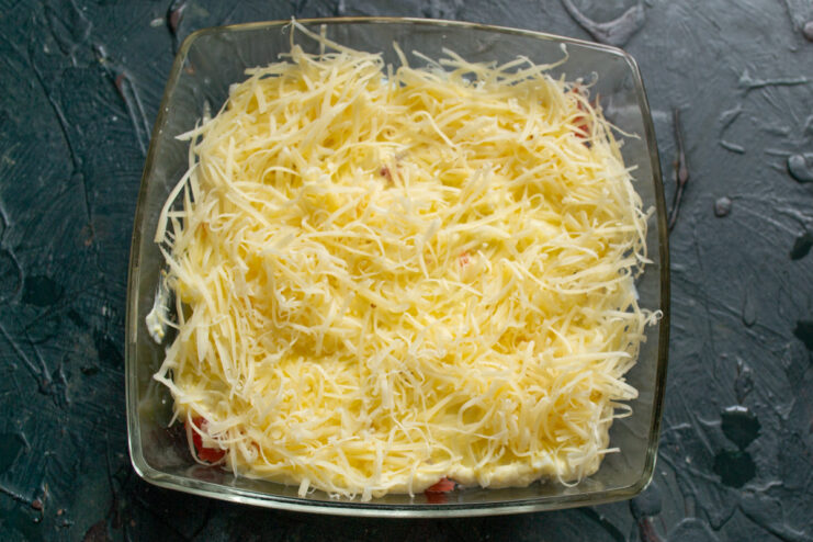 Adding a generous layer of finely grated hard cheese. Sprinkling a thick layer of finely grated hard cheese over the mayonnaise.