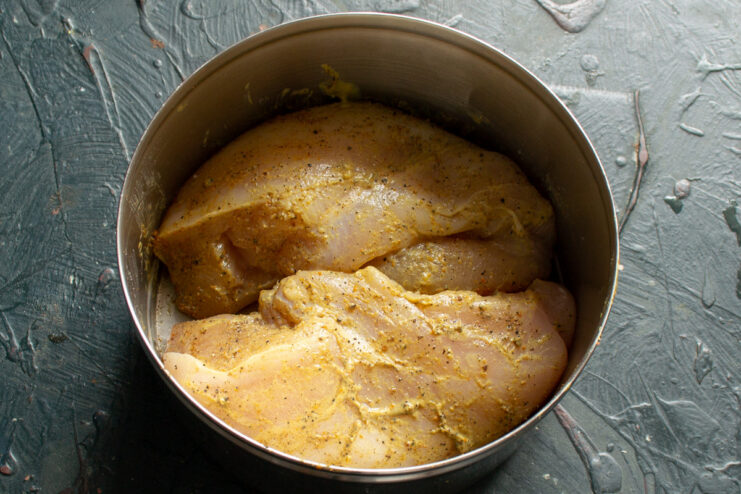Marinating the chicken fillet with spices for extra flavor. Raw chicken fillet being rubbed with a spice mix of salt, mustard, and peppers.