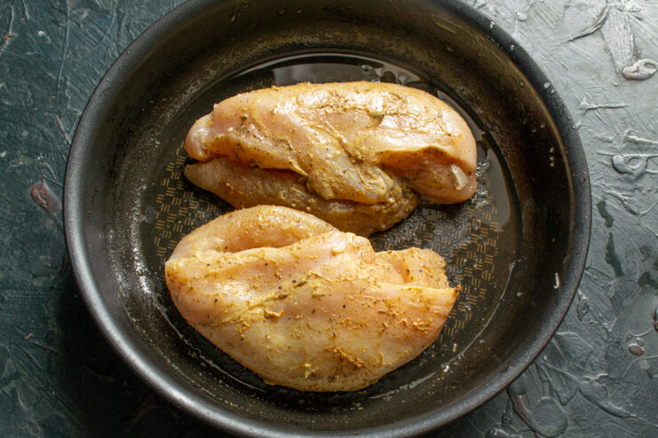 Frying the chicken until it's perfectly golden brown. Marinated chicken fillet sizzling in a pan, getting a golden-brown crust.