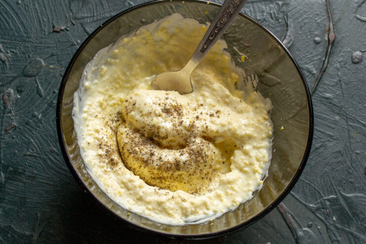Seasoning the mayonnaise-based sauce for the salad. A bowl of mayonnaise-based sauce being seasoned with freshly ground black pepper.
