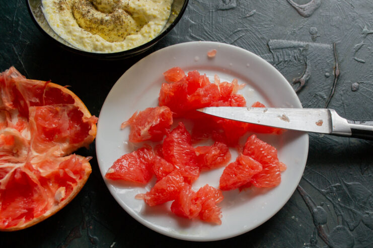 Preparing juicy grapefruit segments for the salad. A hand carving out segments from a halved grapefruit, removing the pith.