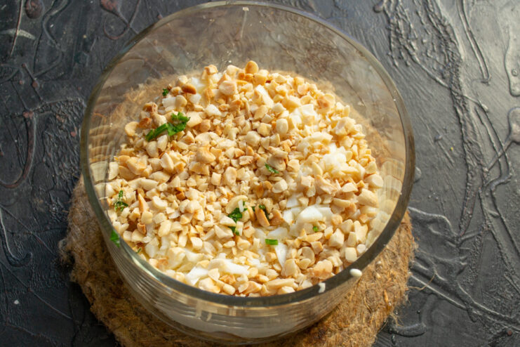 Adding crunchy toasted peanuts to the salad Toasted peanuts being added as the next layer in the salad.