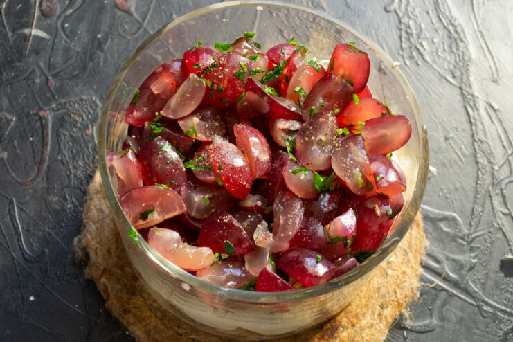 Finishing the salad with fresh grapes and a sprinkle of pepper Final layer of halved red grapes being added to the salad bowl.