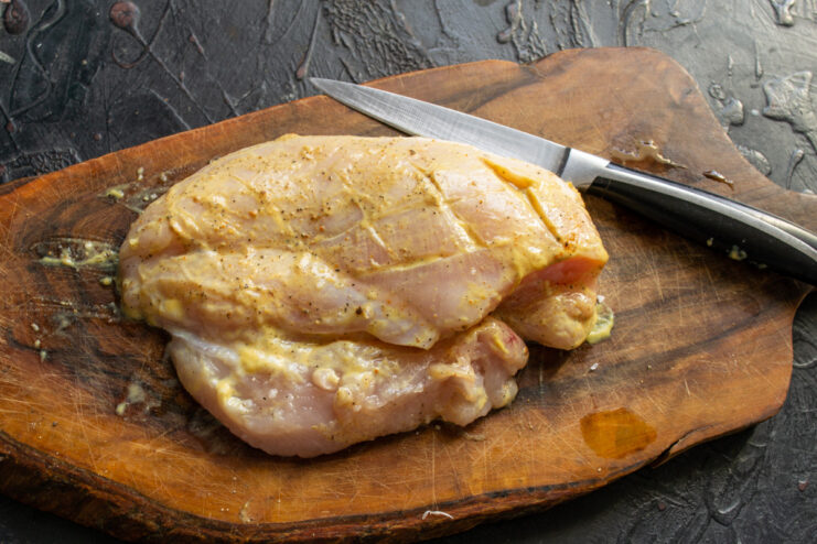 Marinating the chicken breast for maximum flavor Raw chicken breast being rubbed with a marinade of mustard and spices.