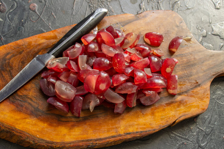 Prepping the sweet grapes for the salad A pile of halved red grapes on a cutting board.