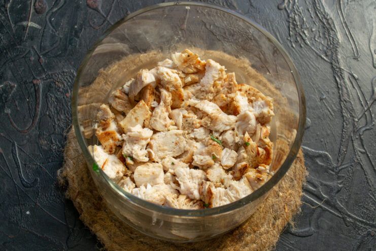 Cutting the cooked chicken into bite-sized pieces Cooked chicken breast being diced into small cubes on a cutting board.