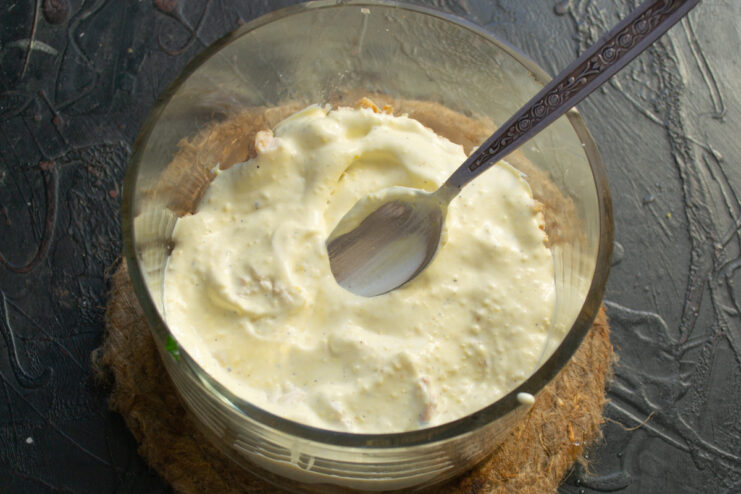 Layering the salad: adding the creamy dressing Layer of diced chicken in a salad bowl being topped with a creamy sauce.