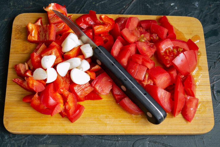 Sliced garlic being added to a bowl of diced tomatoes and red peppers.