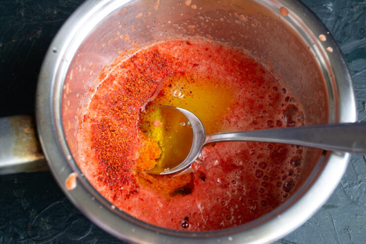 Pouring oil into the pot with the vegetable puree, with spices nearby.