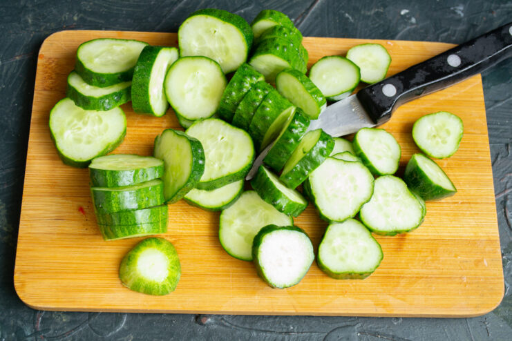 Close-up of fresh cucumbers being sliced into thick rounds on a cutting board.
