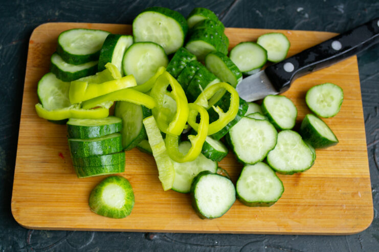 Sliced hot pepper rings being added to a bowl of sliced cucumbers.