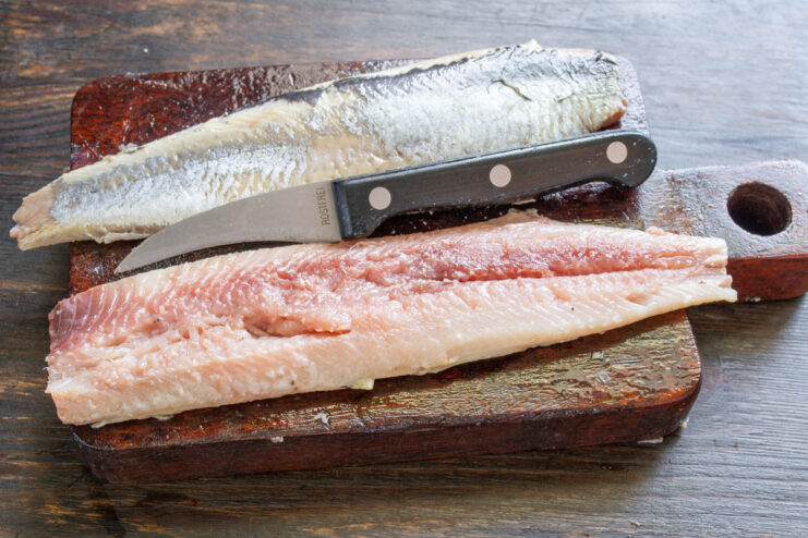 How to Properly Fillet a Salted Herring A whole salted herring being prepared, with a cut along its back to remove the skin.